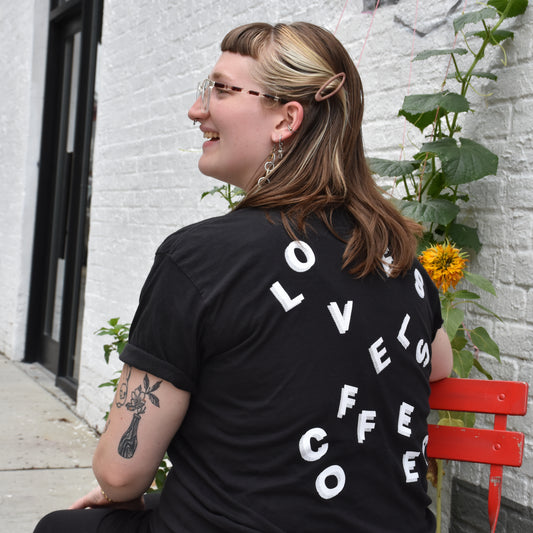 A person showing off the back of a black t-shirt with a stylized Loveless Coffees logo.