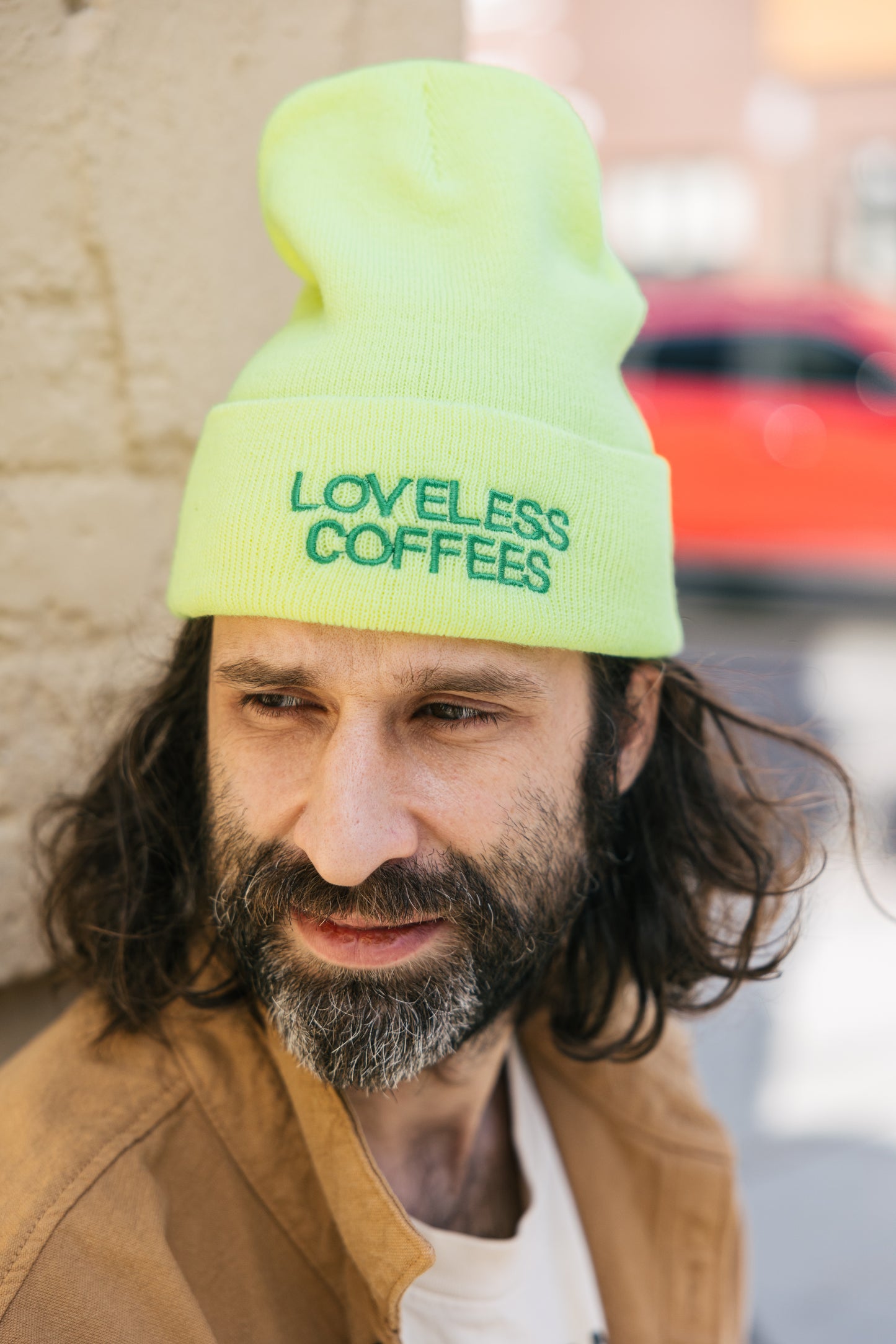 A person wearing a neon yellow beanie with the text 'LOVELESS COFFEES' embroidered on the front.