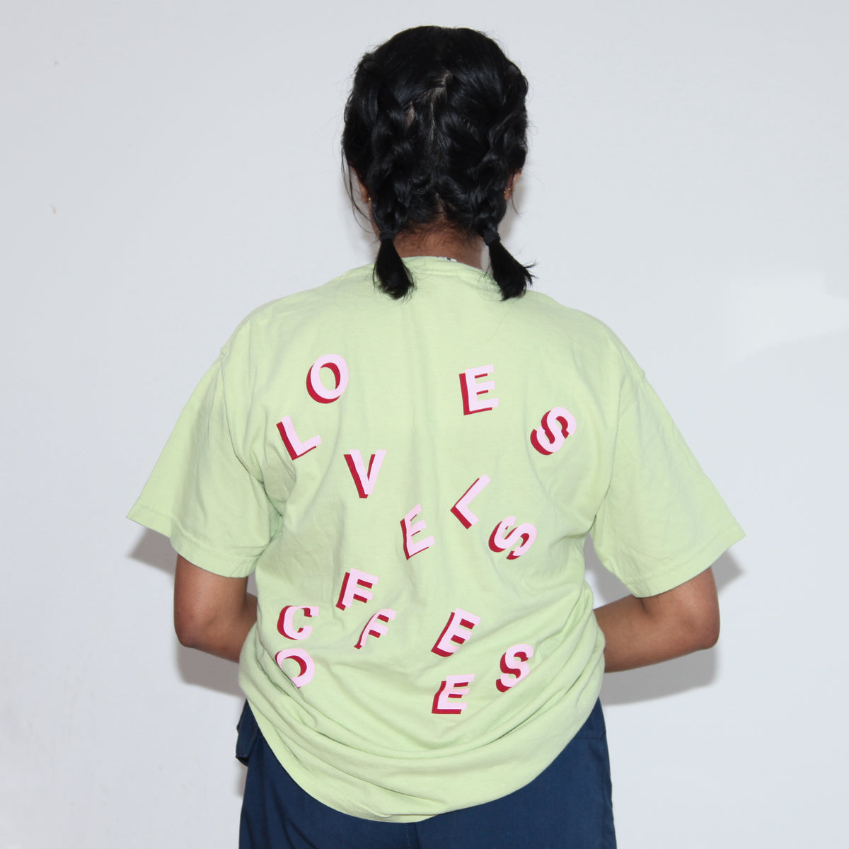 A rear view of a woman wearing light green Loveless Coffees Pocket Tee with stylized red and pink logo