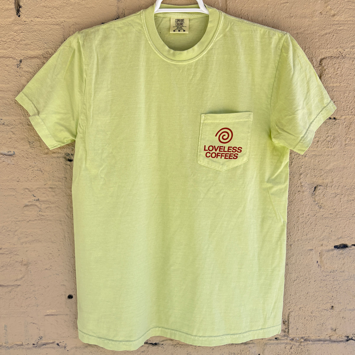 A light green pocket t-shirt with 'LOVELESS COFFEES' text in red on the pocket. 